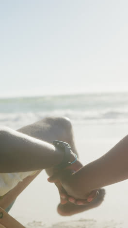 Vertical-video-of-senior-african-american-couple-holding-hands-at-beach,-in-slow-motion