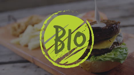 Animation-of-bio-text-on-green-logo-over-white-sauce-pouring-on-vegetarian-cheeseburger