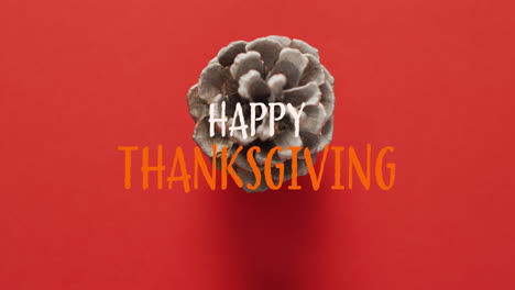 Animation-of-happy-thanksgiving-text-and-pine-cone-on-red-background