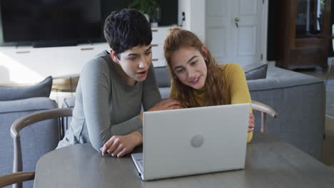 Happy-caucasian-lesbian-couple-sitting,-smiling-and-using-laptop-in-sunny-living-room