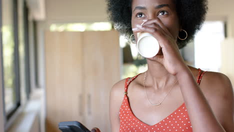 Mujer-De-Negocios-Afroamericana-Informal-Tomando-Café-Y-Usando-Un-Teléfono-Inteligente-En-La-Oficina,-Cámara-Lenta