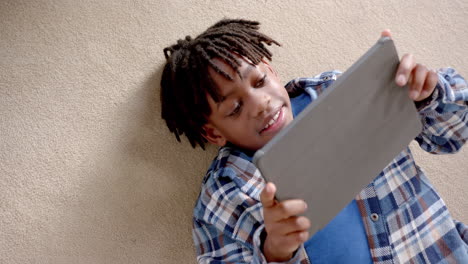 Glücklicher-Afroamerikanischer-Junge-Mit-Tablet,-Das-Zu-Hause-Auf-Dem-Boden-Liegt,-Zeitlupe
