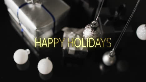 Happy-holidays-text-over-christmas-baubles-and-presents-on-dark-background