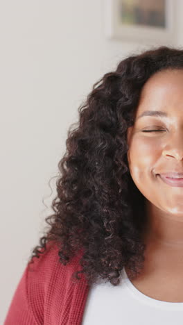 Vertical-video-of-half-face-of-happy-biracial-woman-standing-and-smiling-in-sunny-house