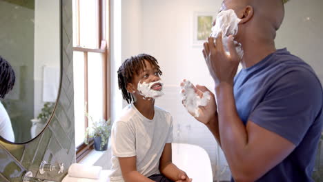 Feliz-Padre-E-Hijo-Afroamericanos-Aplicando-Espuma-De-Afeitar-En-La-Cara-En-El-Baño-De-Casa,-Cámara-Lenta