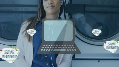 Animation-of-save-energy-text-with-laptop-and-lightning-icons-over-biracial-woman-doing-laundry