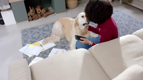 Biracial-woman-with-golden-retriever-dog-using-smartphone-at-home,-slow-motion