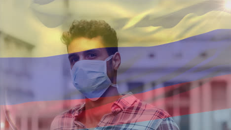 Animation-of-waving-colombia-flag-against-biracial-man-adjusting-his-face-mask-on-the-street