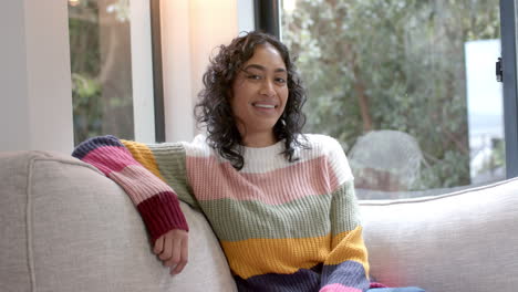 Portrait-of-happy-biracial-woman-sitting-on-sofa-smiling-at-home,-slow-motion