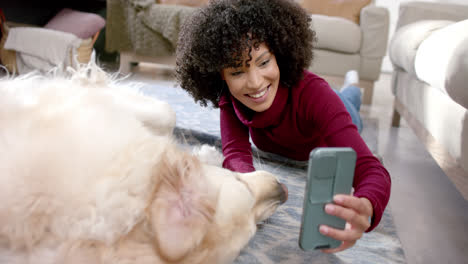 Happy-biracial-woman-taking-photo-with-golden-retriever-dog-using-smartphone-at-home,-slow-motion