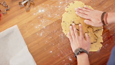 Biracial-man-wearing-christmas-hat,-cutting-christmas-cookies-in-kitchen-at-home,-slow-motion