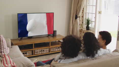 Biracial-family-watching-tv-with-rugby-ball-on-flag-of-france-on-screen