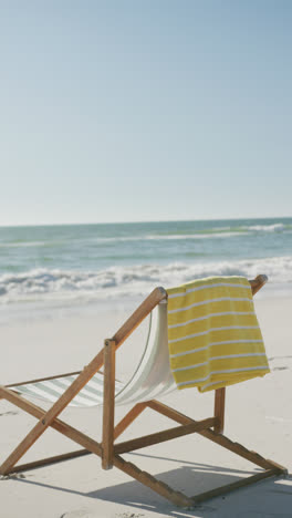 Vertical-video-of-deck-chair-and-towel-on-beach,-in-slow-motion,-with-copy-space