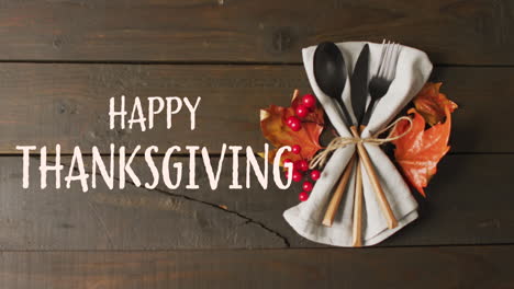 Animation-of-happy-thanksgiving-text-and-cutlery-and-autumn-leaves-over-wooden-background