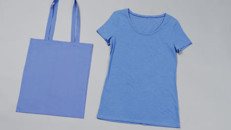 Close-up-of-blue-bag-and-t-shirt-on-grey-background,-with-copy-space,-slow-motion