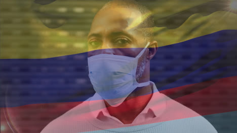 Animation-of-waving-colombia-flag-over-portrait-of-african-american-man-wearing-face-mask-on-street