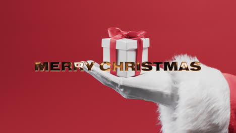 Frohe-Weihnachten-Text-In-Gold-über-Hand-Von-Santa-Claus-Hält-Geschenk-Auf-Rotem-Hintergrund