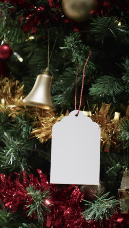 Vertical-video-of-christmas-tree-withdecorations-and-white-tag-with-copy-space