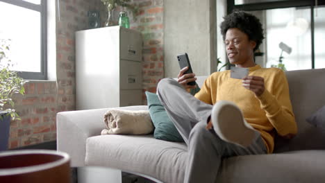Glücklicher-Afroamerikanischer-Mann,-Der-Auf-Dem-Sofa-Sitzt-Und-Sein-Smartphone-Zum-Online-Shopping-Zu-Hause-Nutzt,-Zeitlupe