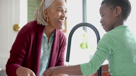 Glückliche-Afroamerikanische-Großmutter-Und-Enkel-Beim-Gemüsewaschen-In-Der-Küche,-Zeitlupe