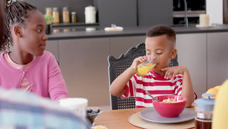 African-american-brother-and-sister-eating-breakfast-at-table-in-kitchen,-slow-motion