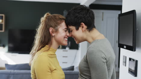 Feliz-Pareja-De-Lesbianas-Caucásicas-Abrazándose,-Sonriendo-Y-Riendo-En-La-Soleada-Cocina