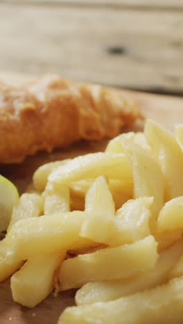 Video-of-fish-and-chips-with-lemon-wedge-on-wooden-board,-on-rustic-table