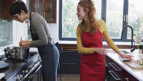 Happy-caucasian-lesbian-couple-preparing-food-and-embracing-in-sunny-kitchen