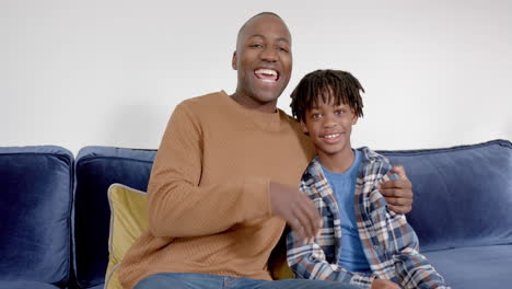 Portrait-of-happy-african-american-father-and-son-embracing-on-sofa-at-home,-slow-motion