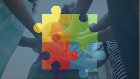 Animation-of-connected-puzzle-pieces-over-low-angle-view-of-diverse-children-putting-hands-together