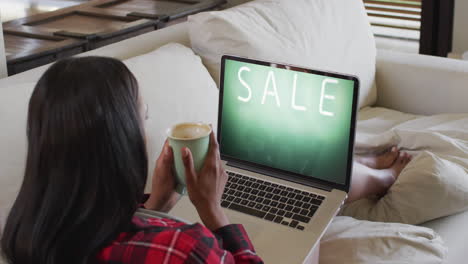 Biracial-woman-using-laptop-on-couch-at-home-online-shopping-during-sale,-slow-motion