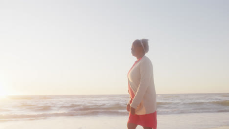 Happy-senior-african-american-woman-walking-at-beach,-in-slow-motion,-with-copy-space