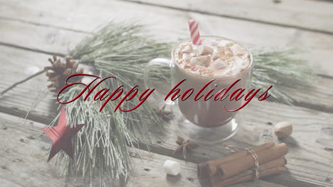 Happy-holidays-text-in-red-over-christmas-decorations-and-hot-chocolate-with-marshmallows