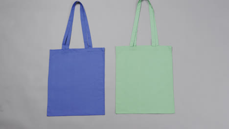 Close-up-of-blue-and-green-bags-on-grey-background,-with-copy-space,-slow-motion