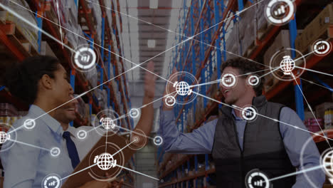 Animation-of-network-of-connections-with-icons-over-diverse-business-people-highfiving-in-warehouse