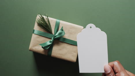 Video-of-christmas-presents-and-hand-holding-white-tag-with-copy-space-on-green-background