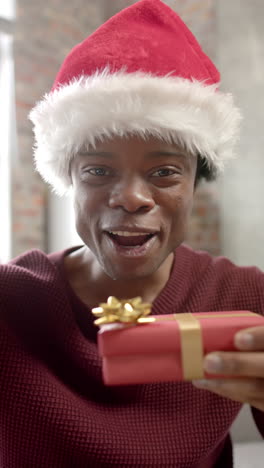 Vertical-video-of-african-american-man-wearing-santa-hat-having-video-call-at-home,-slow-motion