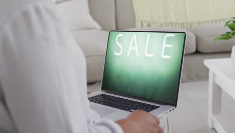 Biracial-woman-using-laptop-at-home-online-shopping-during-sale,-slow-motion