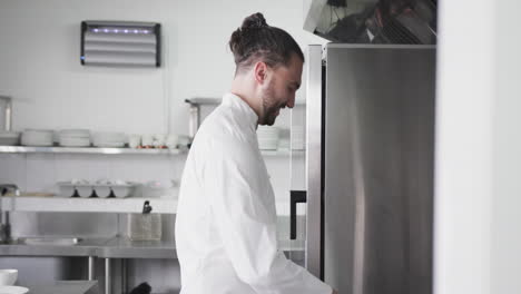 Happy-caucasian-male-chef-with-hair-bun-working-in-restaurant-kitchen,-copy-space,-slow-motion