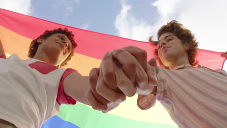 Happy-diverse-gay-male-couple-holding-rainbow-lgbt-flag-and-holding-hands-at-home,-slow-motion