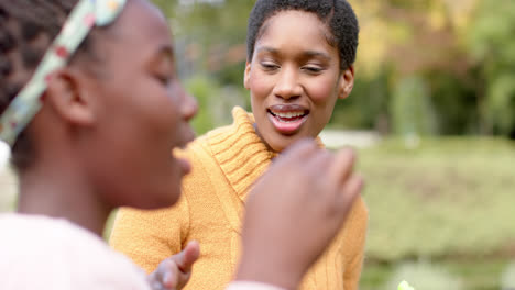 Happy-african-american-mother-and-daughter-blowing-bubbles-in-sunny-garden