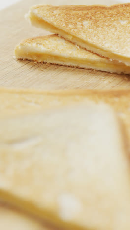 Video-of-slices-of-toasted-cheese-white-bread-sandwiches-on-wooden-chopping-board-background