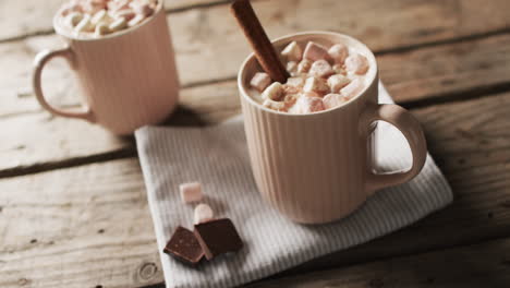 Video-of-mugs-of-chocolate-with-marshmallows,-decorations-and-copy-space-on-wooden-background