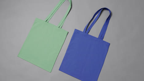 Close-up-of-green-and-blue-bags-on-grey-background,-with-copy-space,-slow-motion