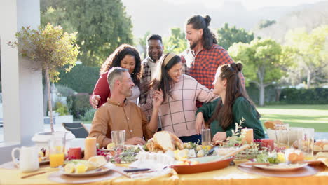 Happy-diverse-male-and-female-friends-posing-on-thanksgiving-celebration-meal-in-sunny-garden