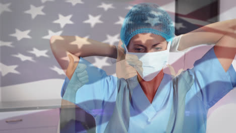 Animation-of-waving-usa-flag-against-biracial-female-surgeon-wearing-surgical-mask-at-hospital