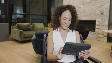 Portrait-of-biracial-businesswoman-in-wheelchair-using-tablet-in-office-and-smiling,-in-slow-motion