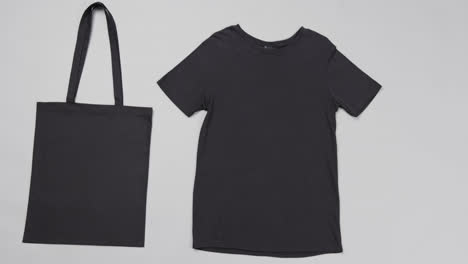 Close-up-of-black-bag-and-t-shirt-on-grey-background,-with-copy-space,-slow-motion