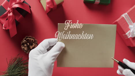 Frohe-Weihnachten-Texto-Sobre-Papá-Noel-Escribiendo-En-Un-Sobre-Sobre-Fondo-Rojo