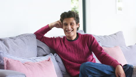 Portrait-of-happy-biracial-man-sitting-on-sofa-at-home,-slow-motion